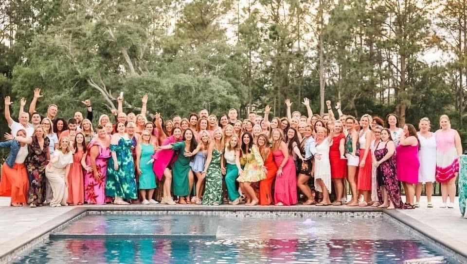 Large team celebrating poolside in colorful dresses